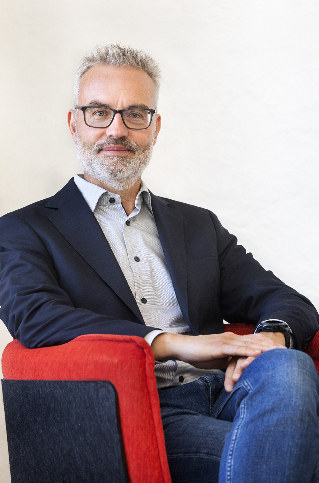 Mikael Larsson sitter i en röd fåtölj mot en ljus vägg.